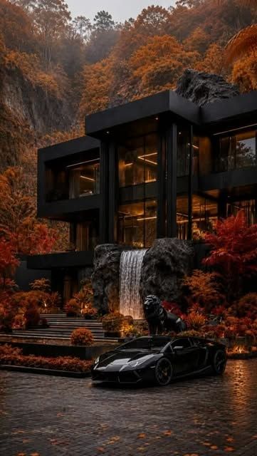 Sonbahar ağaçlarıyla çevrili, geniş camlı siyah cepheli villa ve önündeki şelale
