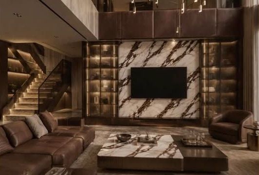 Kahve damarlı mermer TV duvarı, aydınlatmalı vitrinler, ahşap merdiven ve deri koltuklu dubleks salon